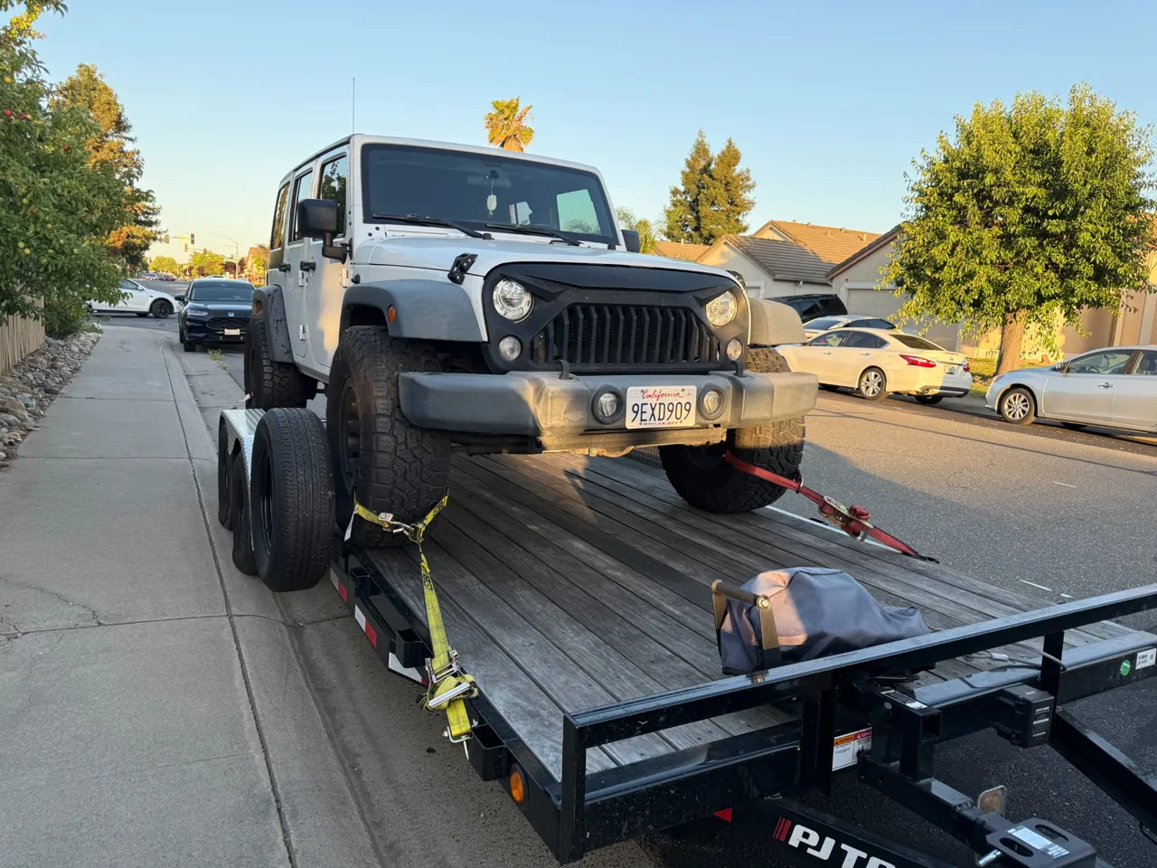 White Jeep on a trailer in a residential neighborhood