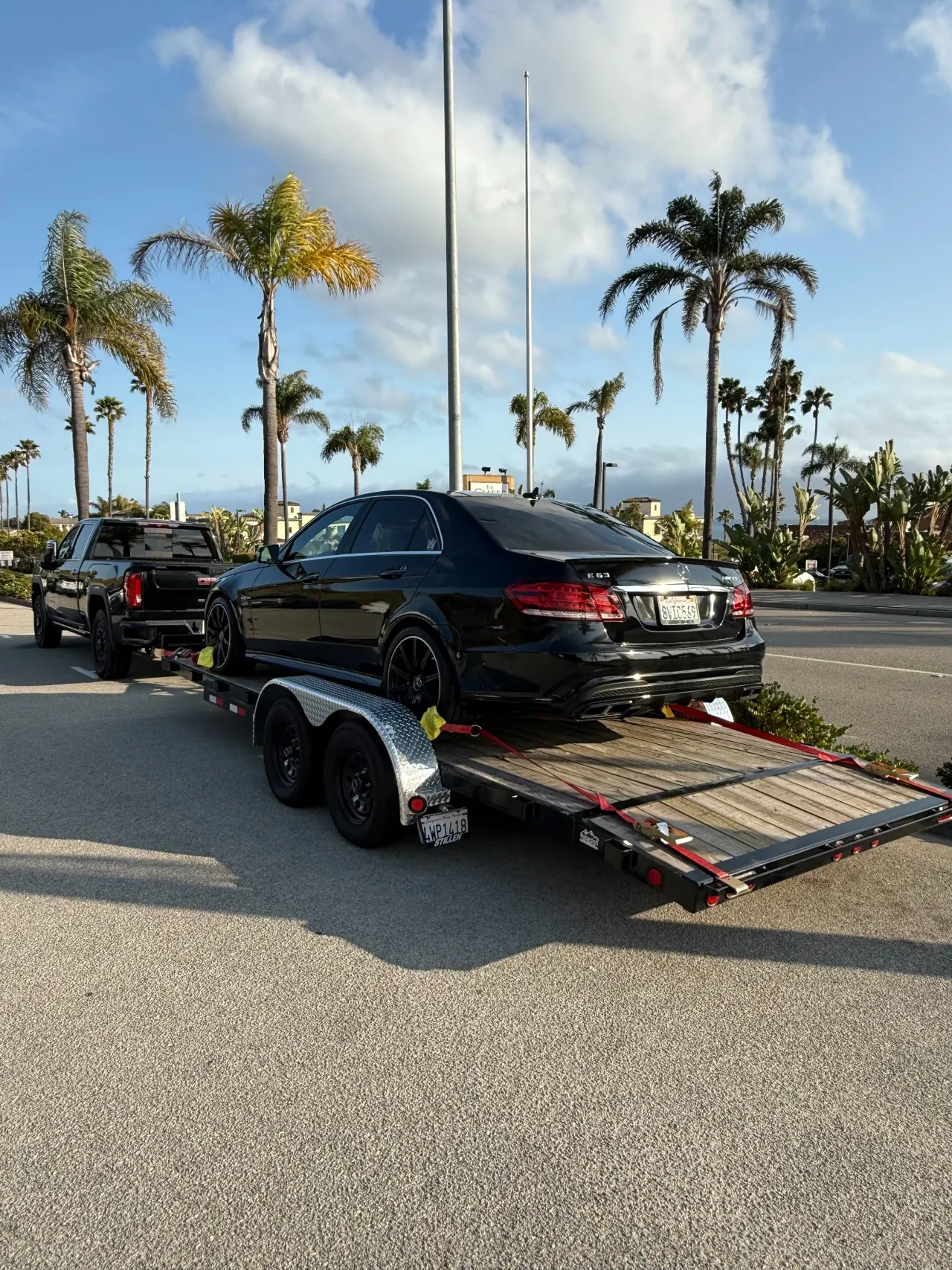 Black Mercedes sedan on a trailer along a palm-lined street
