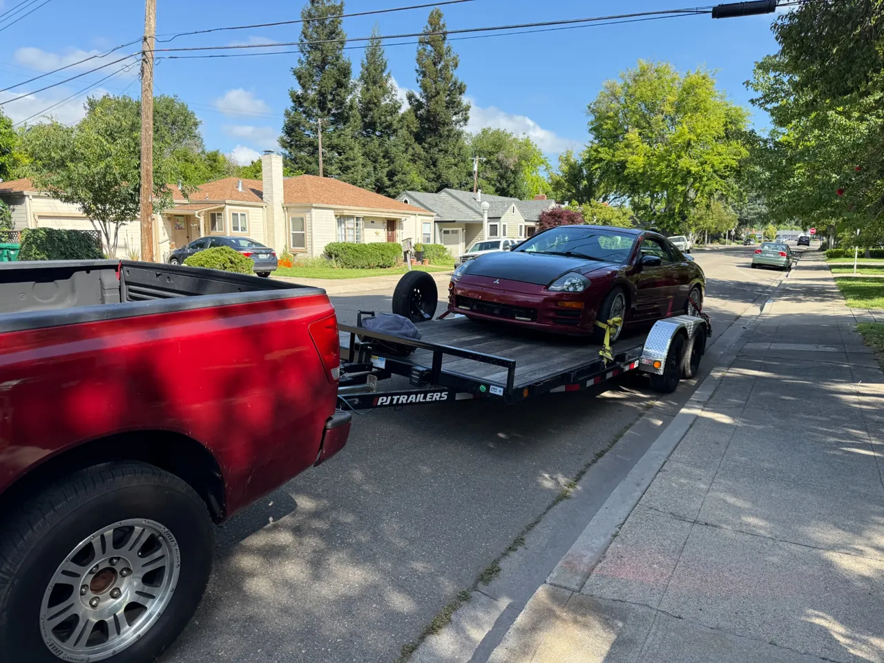 Red sedan loaded on a trailer behind a red pickup